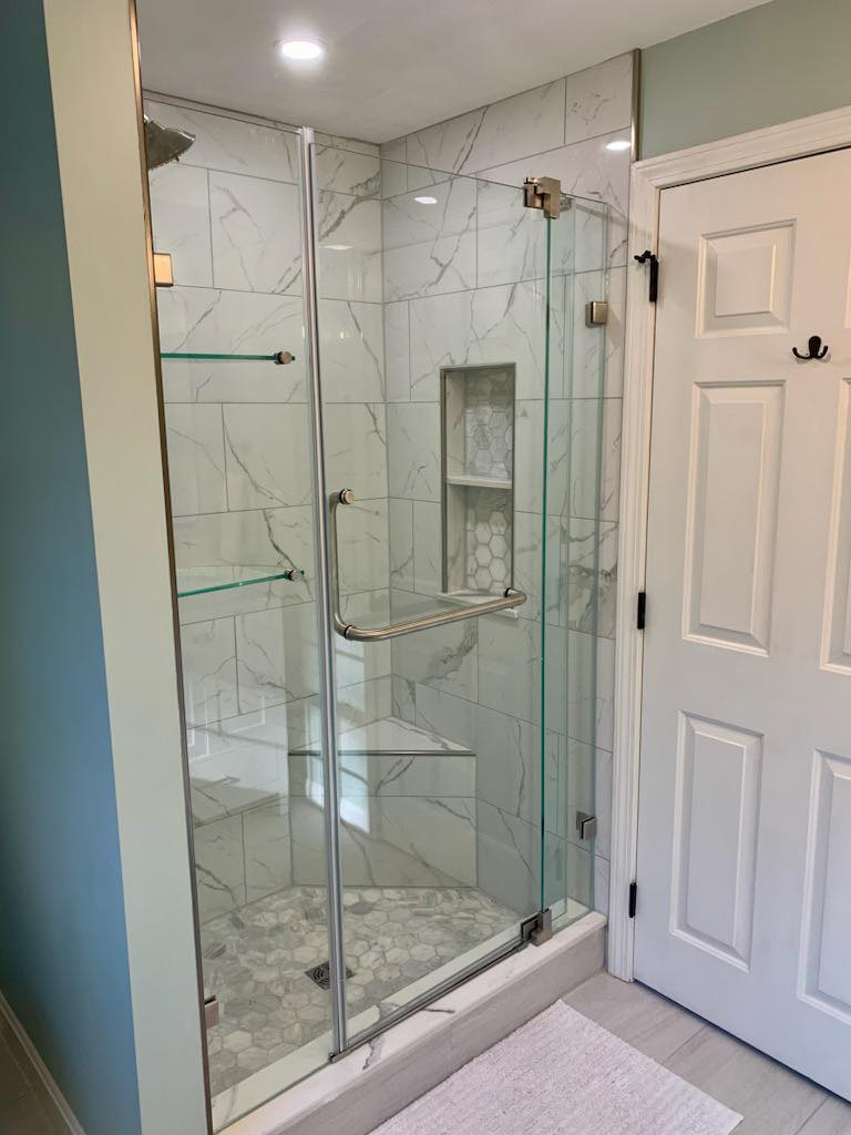 A bathroom with a glass shower door and a white door.