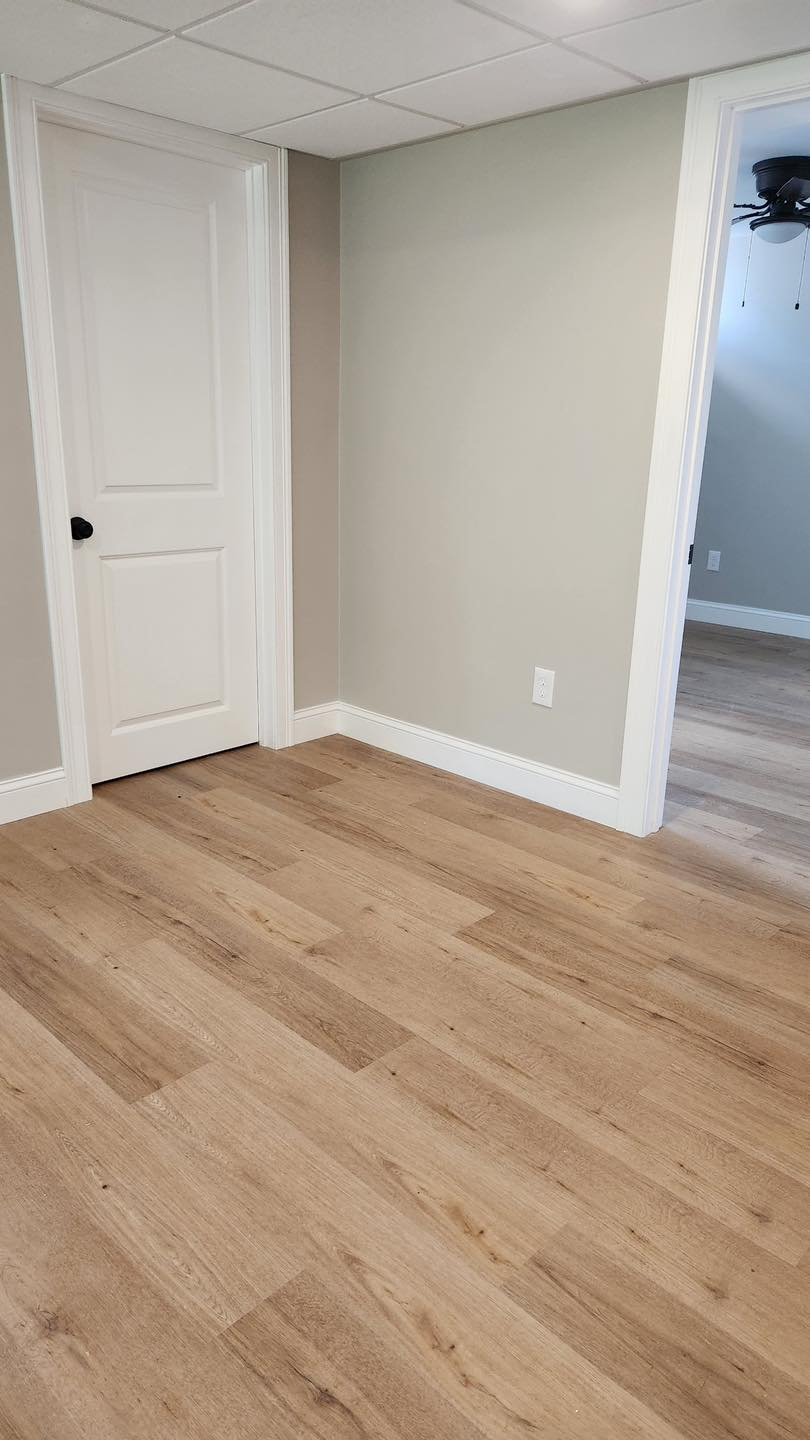 A room with hardwood floors and a door in a basement.