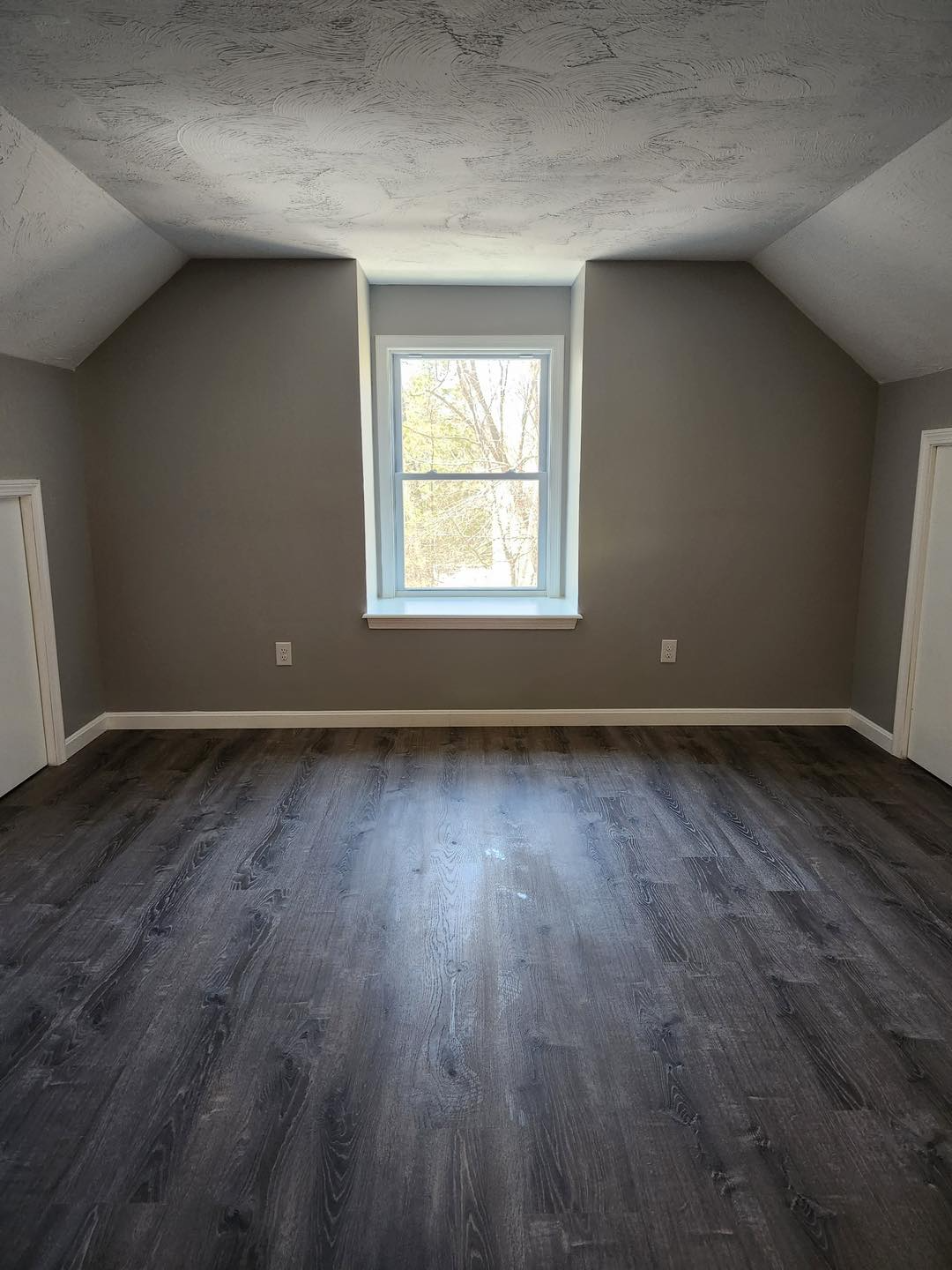 An empty room with hardwood floors and a window.