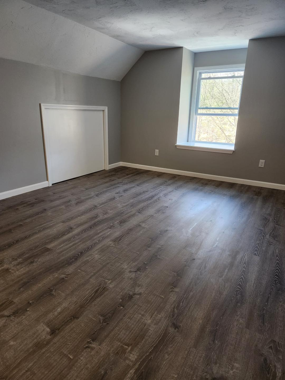 An empty room with hardwood floors and a window.