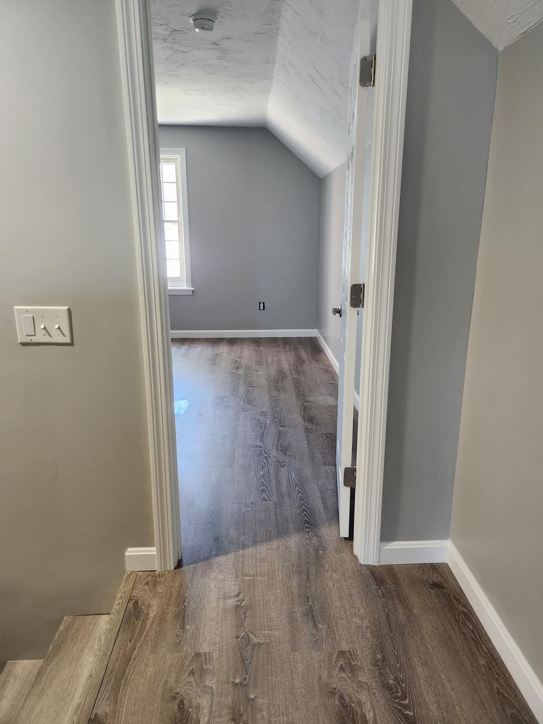 A hallway leading to a bedroom with hardwood floors and stairs.