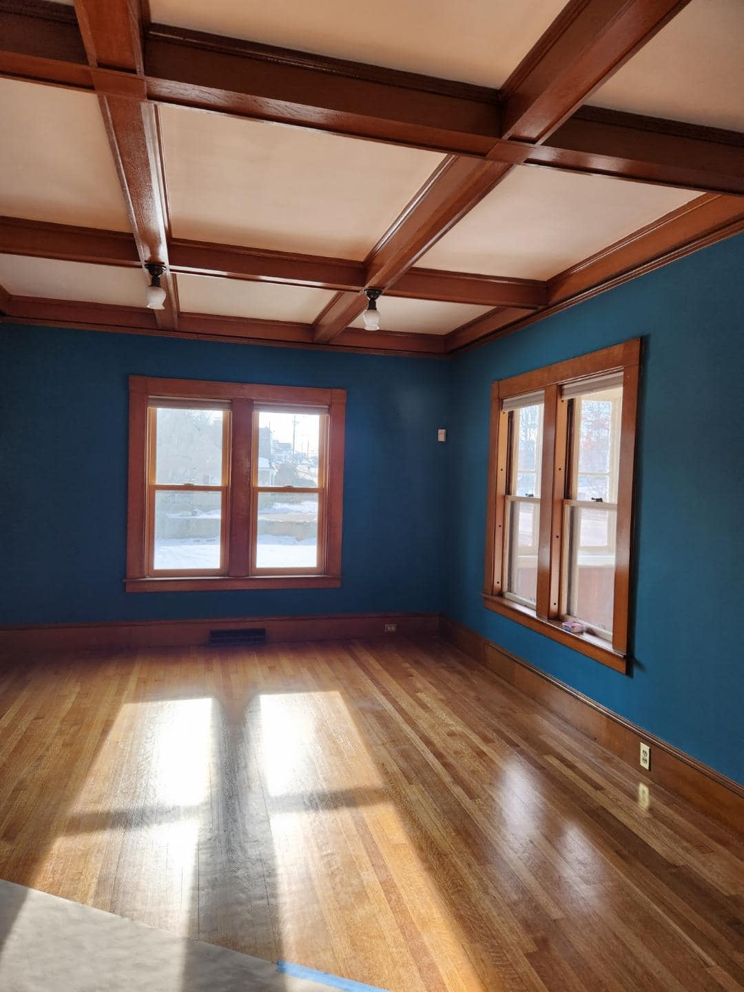 An empty living room with blue walls and hardwood floors.