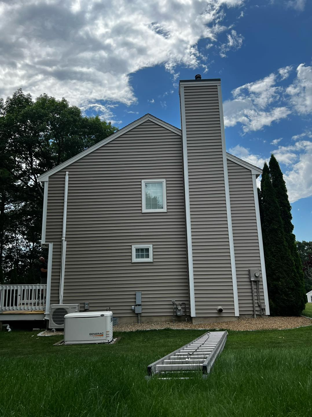 The back of a house with a chimney and a ladder in the grass.
