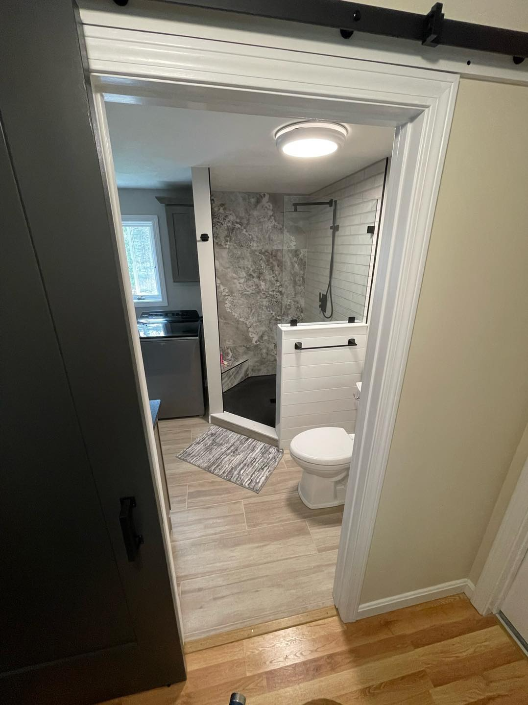 A bathroom with a toilet , shower and sliding barn door.