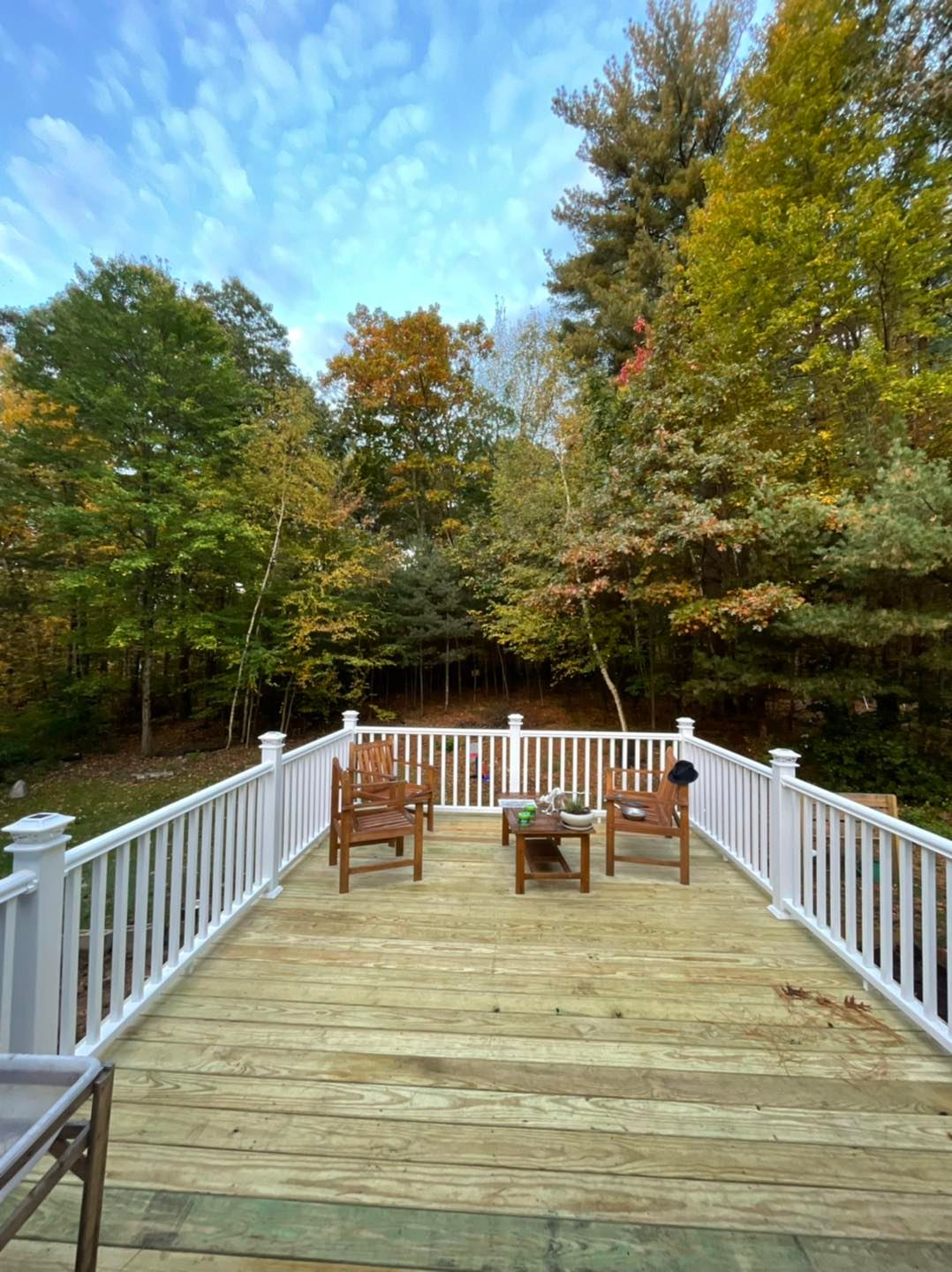 A wooden deck with chairs and a table on it surrounded by trees.
