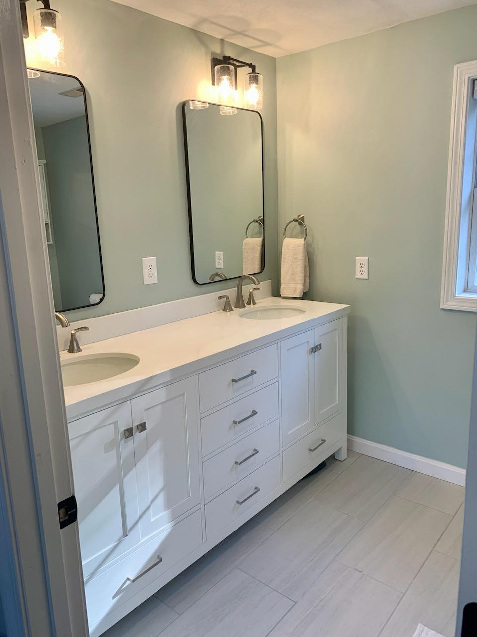 A bathroom with two sinks , two mirrors , and a window.