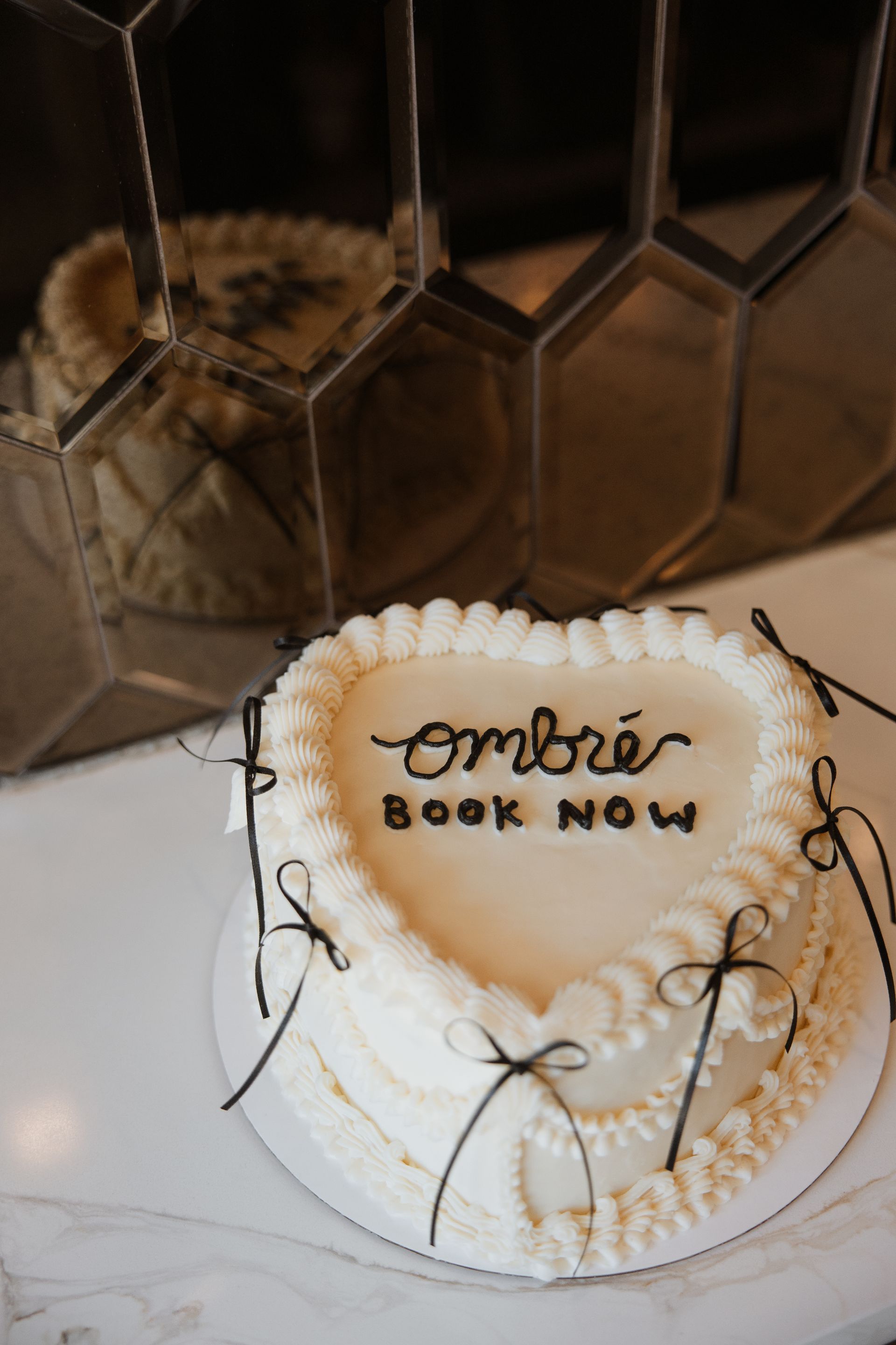 Small white frosted cake with gold lettering on a plate, decorated with gold accents and pearl-like details.