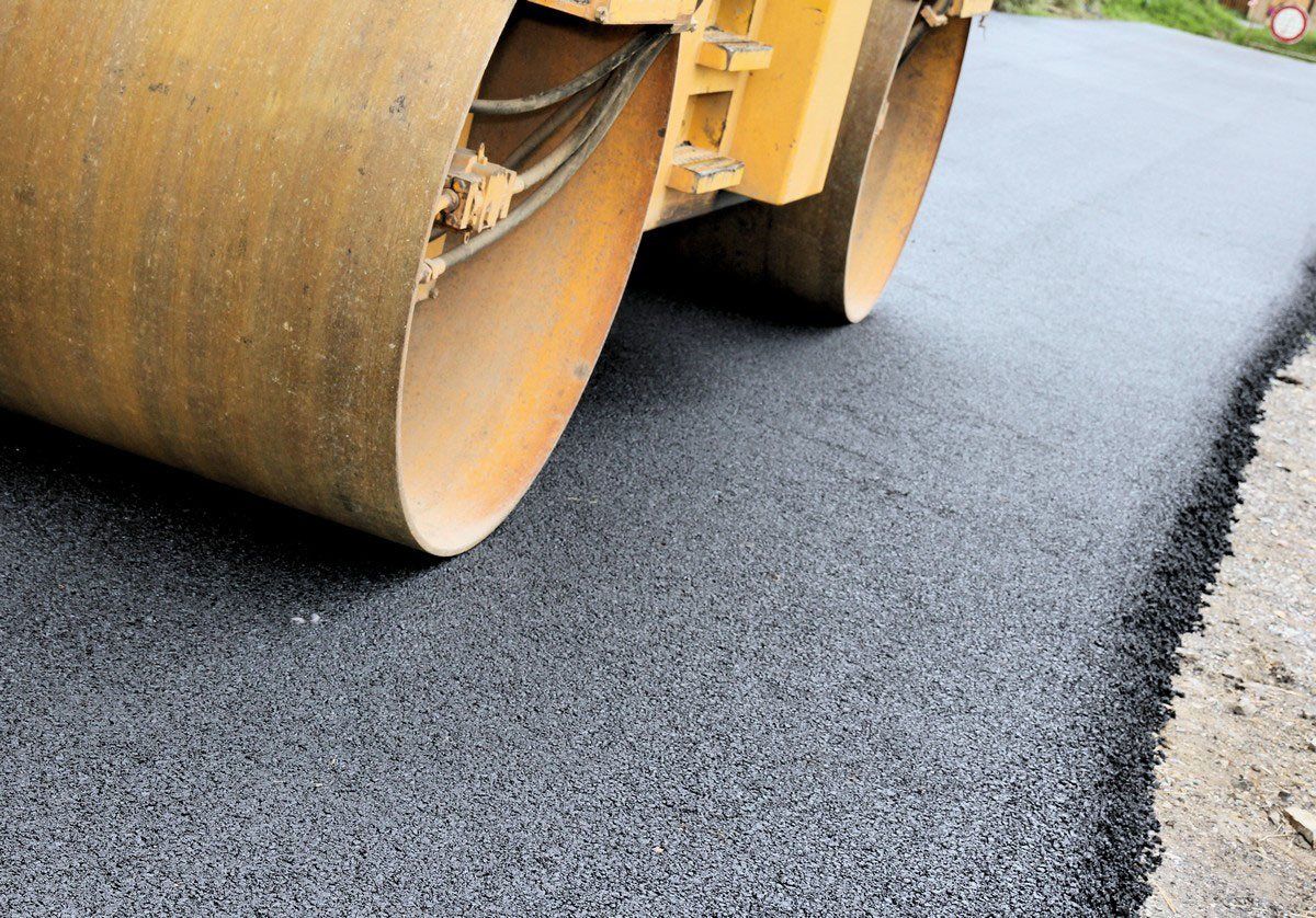 A close-up view of a yellow construction roller compacting a freshly laid asphalt road.
