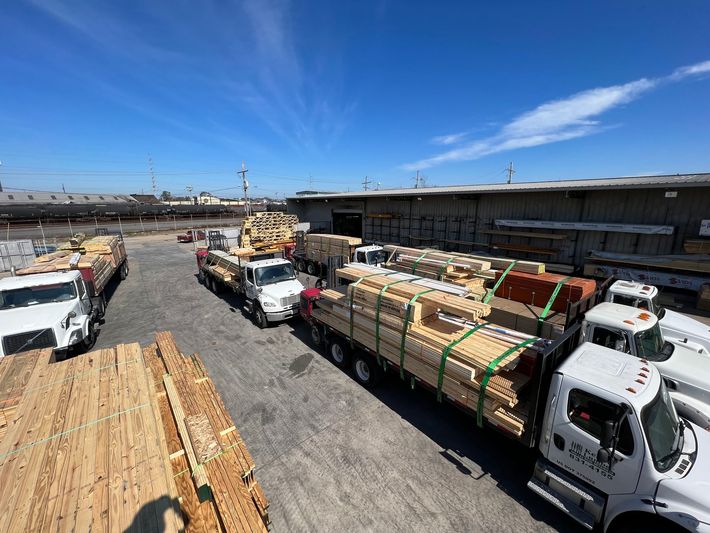 A bunch of trucks are parked in a lot filled with wood.