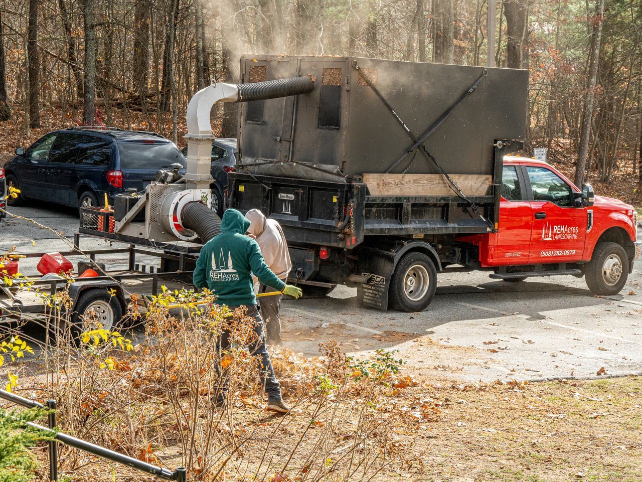 Red pickup truck and black work truck by a wooded roadside, with people handling equipment and debris.
