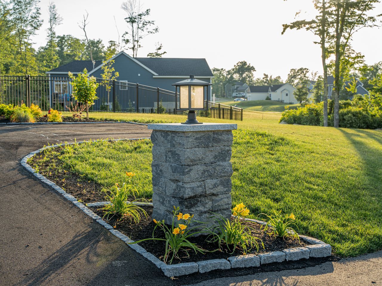 Landscaped driveway with stone lantern, curved flower bed, and modern house at sunset