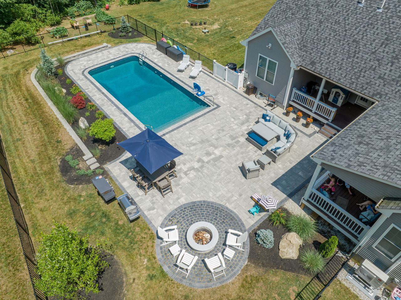 Aerial view of a backyard with a rectangular pool, patio furniture, fire pit, and house deck.