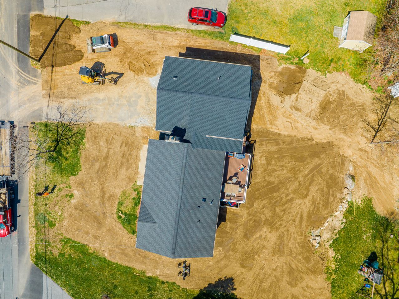 Aerial view of a house with a dark roof, yard, driveway, and two parked cars nearby.