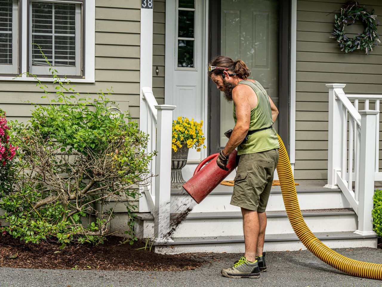 Person using a red leaf blower to clear steps outside a house, with yellow hose on the porch.