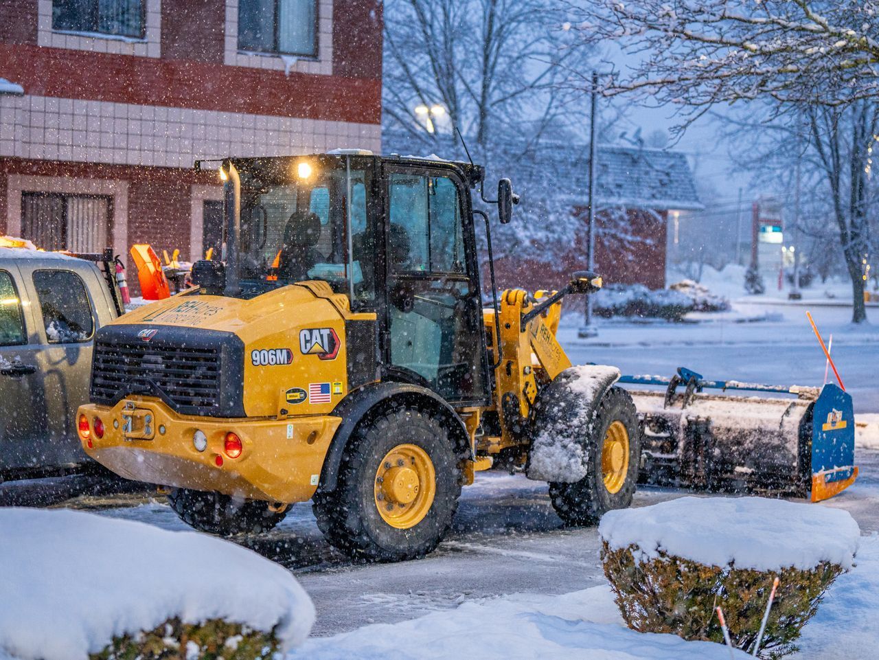 Yellow front loader clearing snow on a residential street during snowfall.