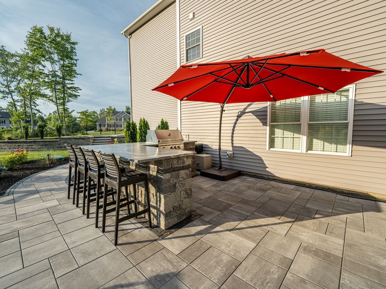 Patio with red umbrella, outdoor bar, and black chairs beside a beige house