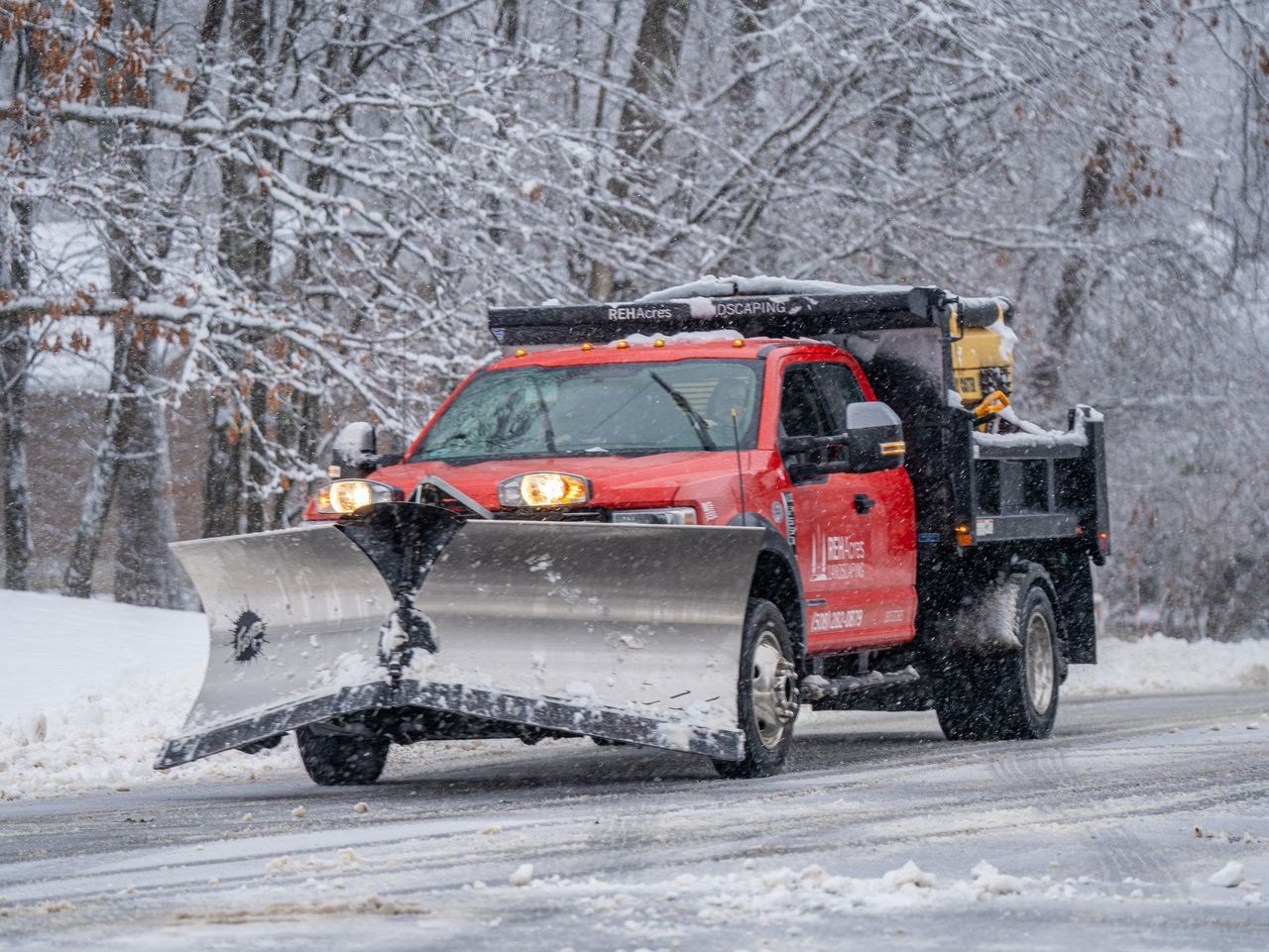 Red snowplow truck clearing a snowy road in a winter forest