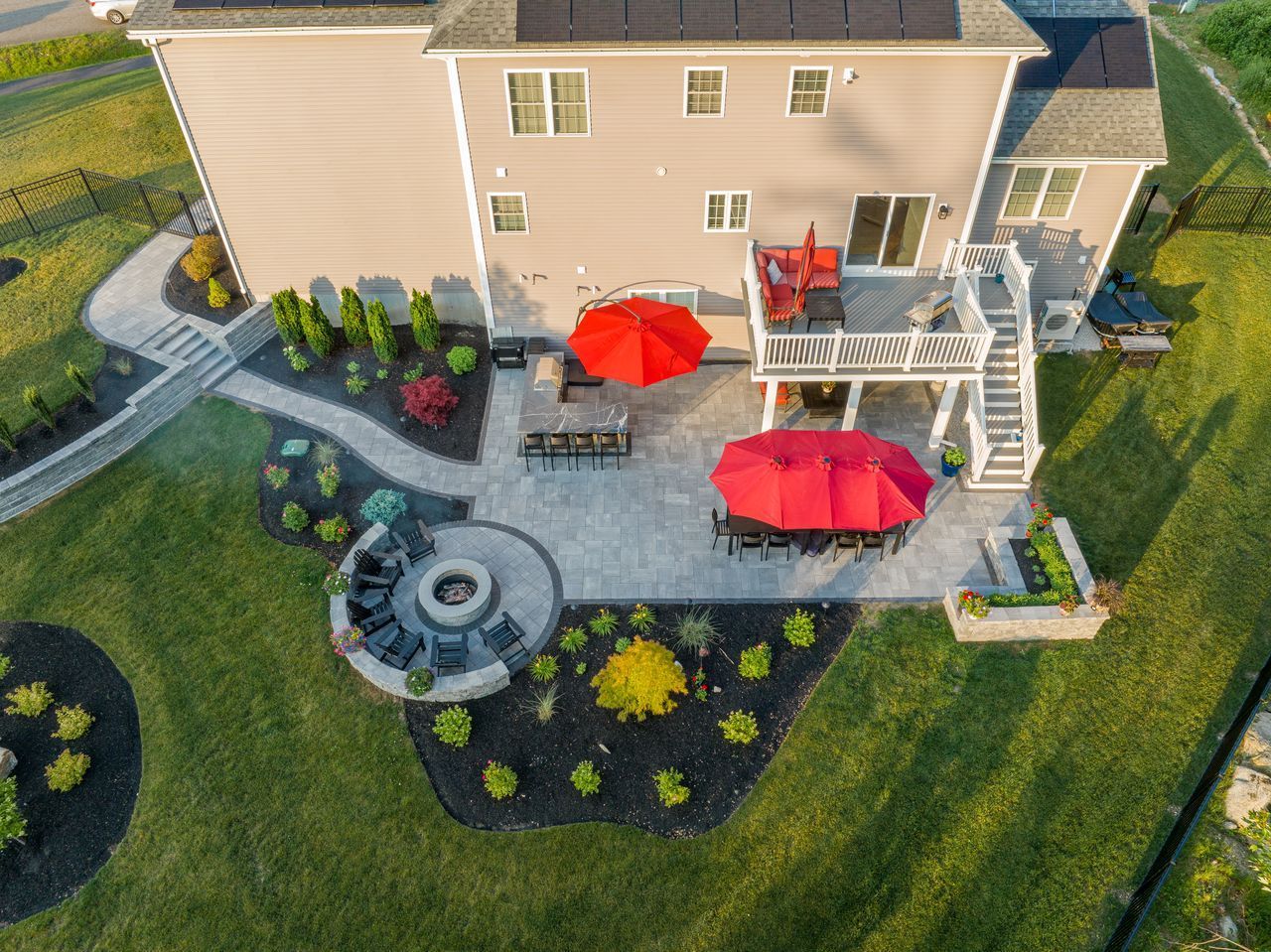 Backyard patio with red umbrellas, fire pit seating, landscaped garden, and a house deck