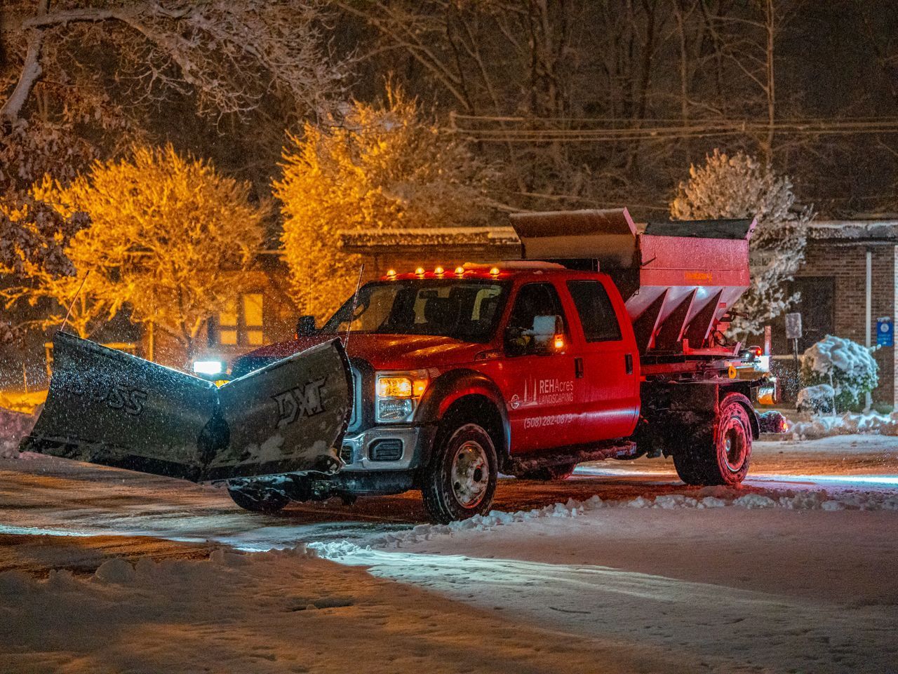 Red snowplow truck clearing snow on a lit residential street at night