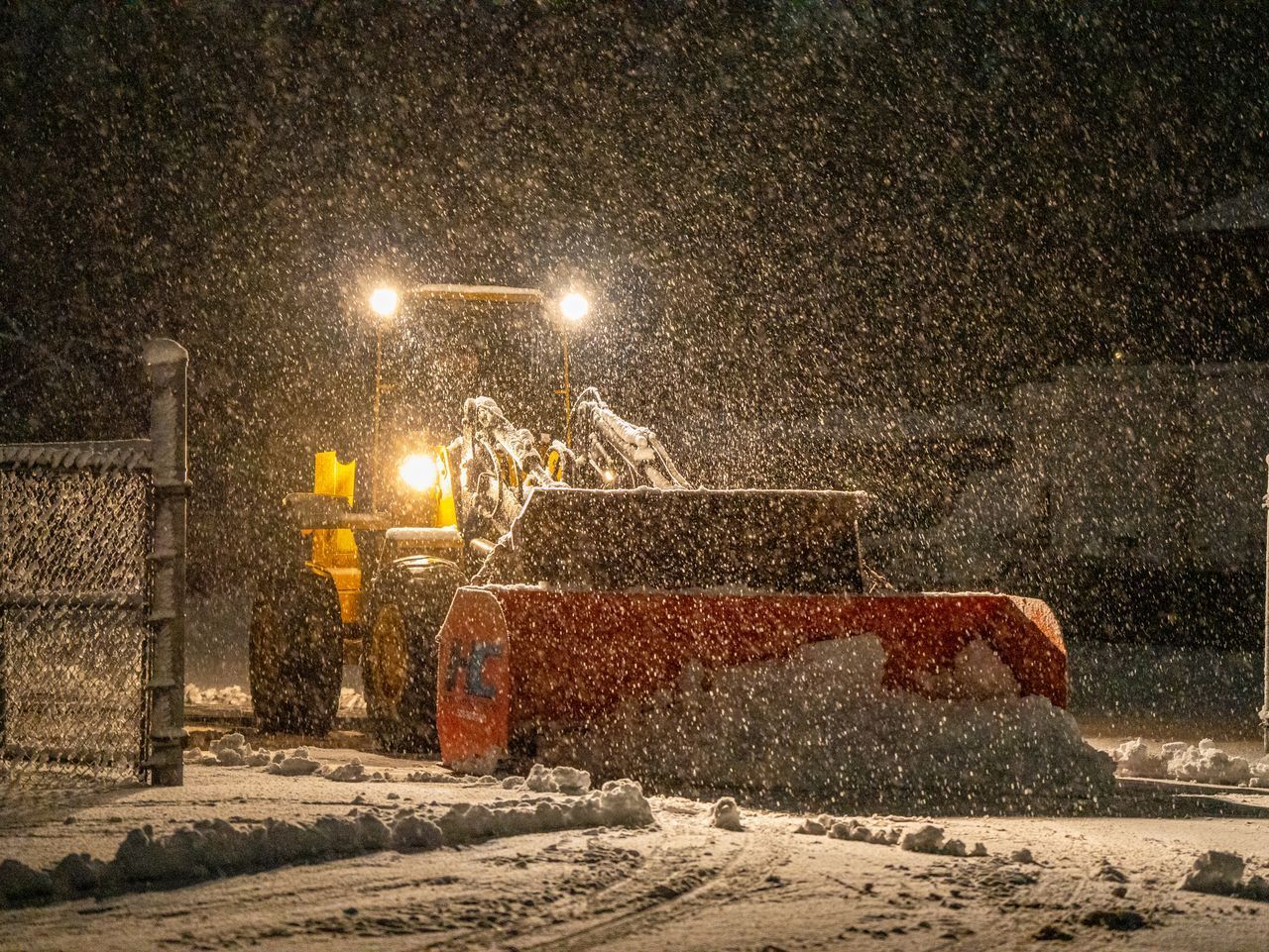 Snowplow clearing a snowy road at night, headlights glowing in falling snow