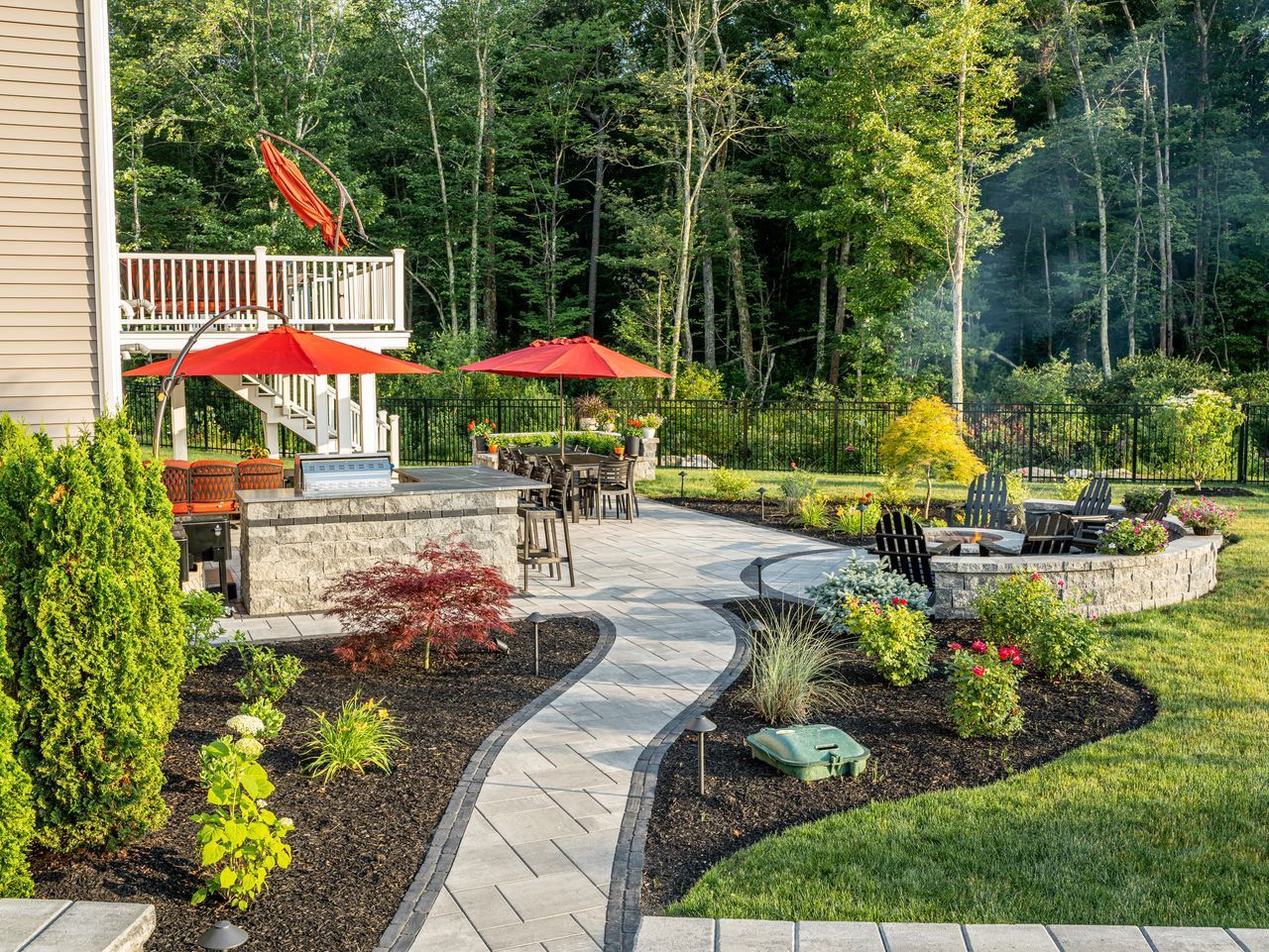 Backyard patio with red umbrellas, stone walkway, and landscaped garden beside a house