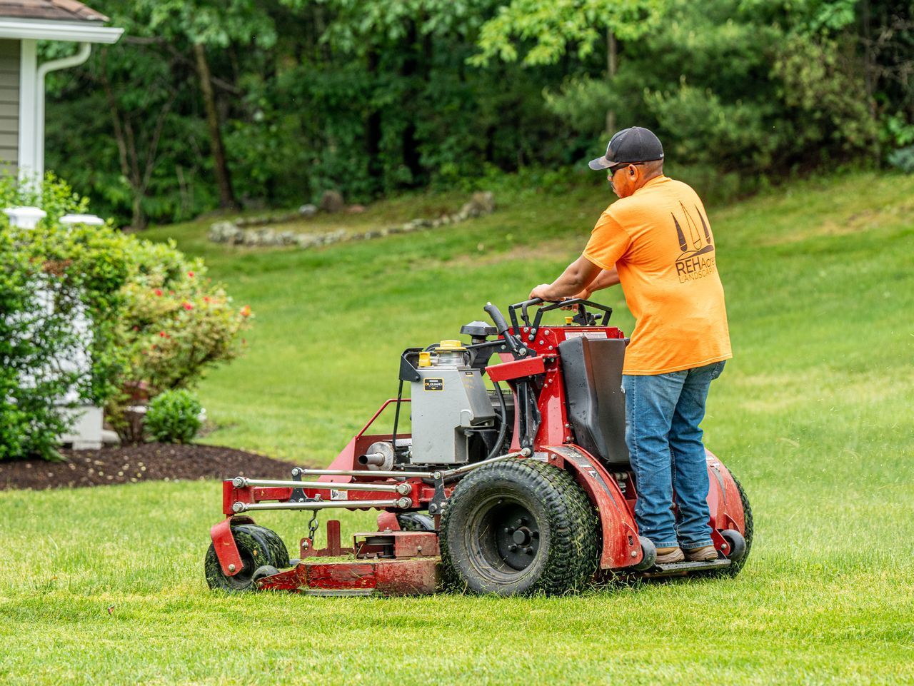 Worker in orange shirt operating a red lawn mower on a green lawn.