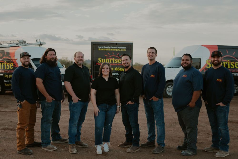 A group of eight people stand in front of vans with Sunrise logo. They are outdoors with a sunset backdrop.