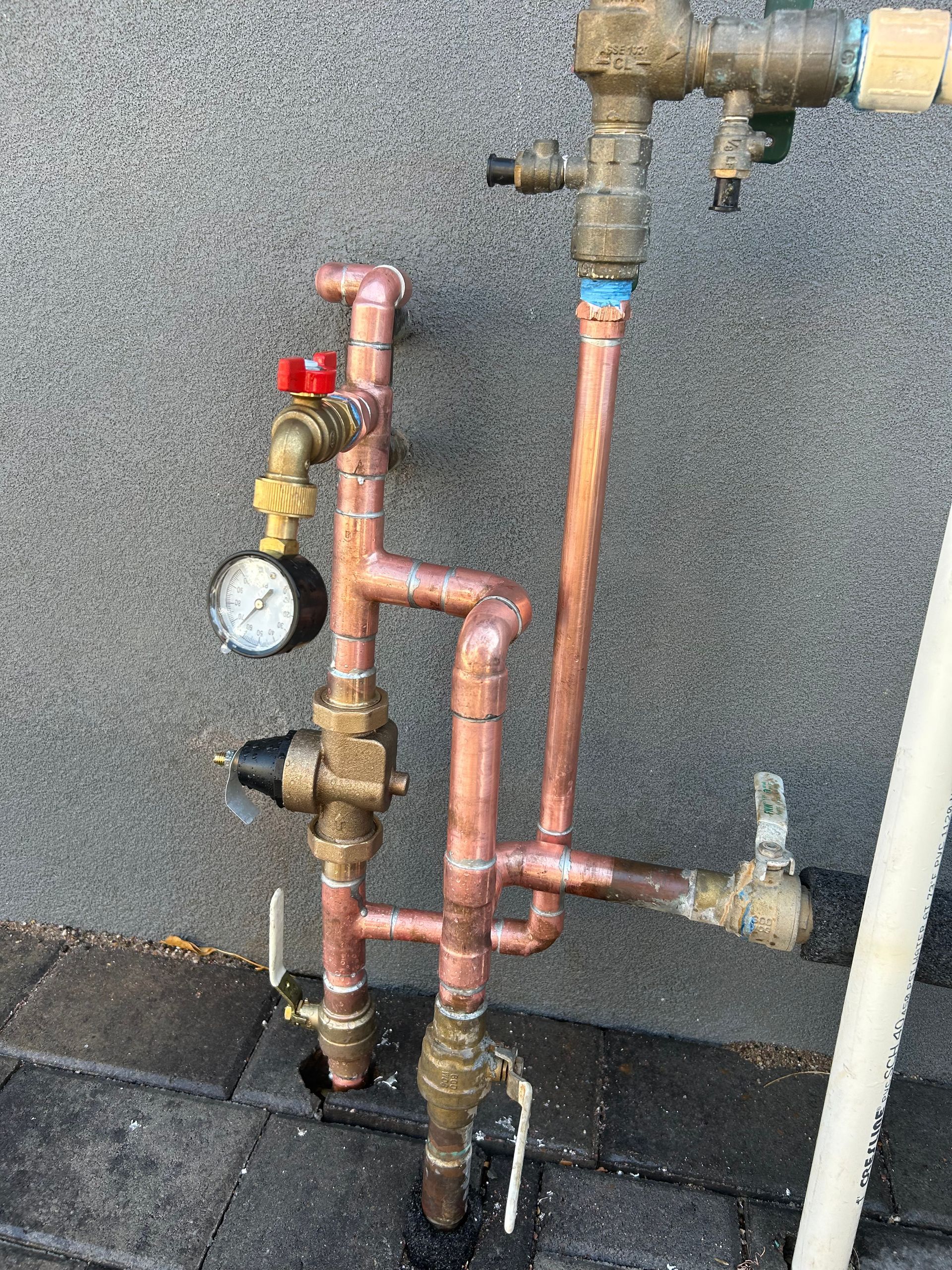 Copper plumbing with gauges and valves against a gray wall.