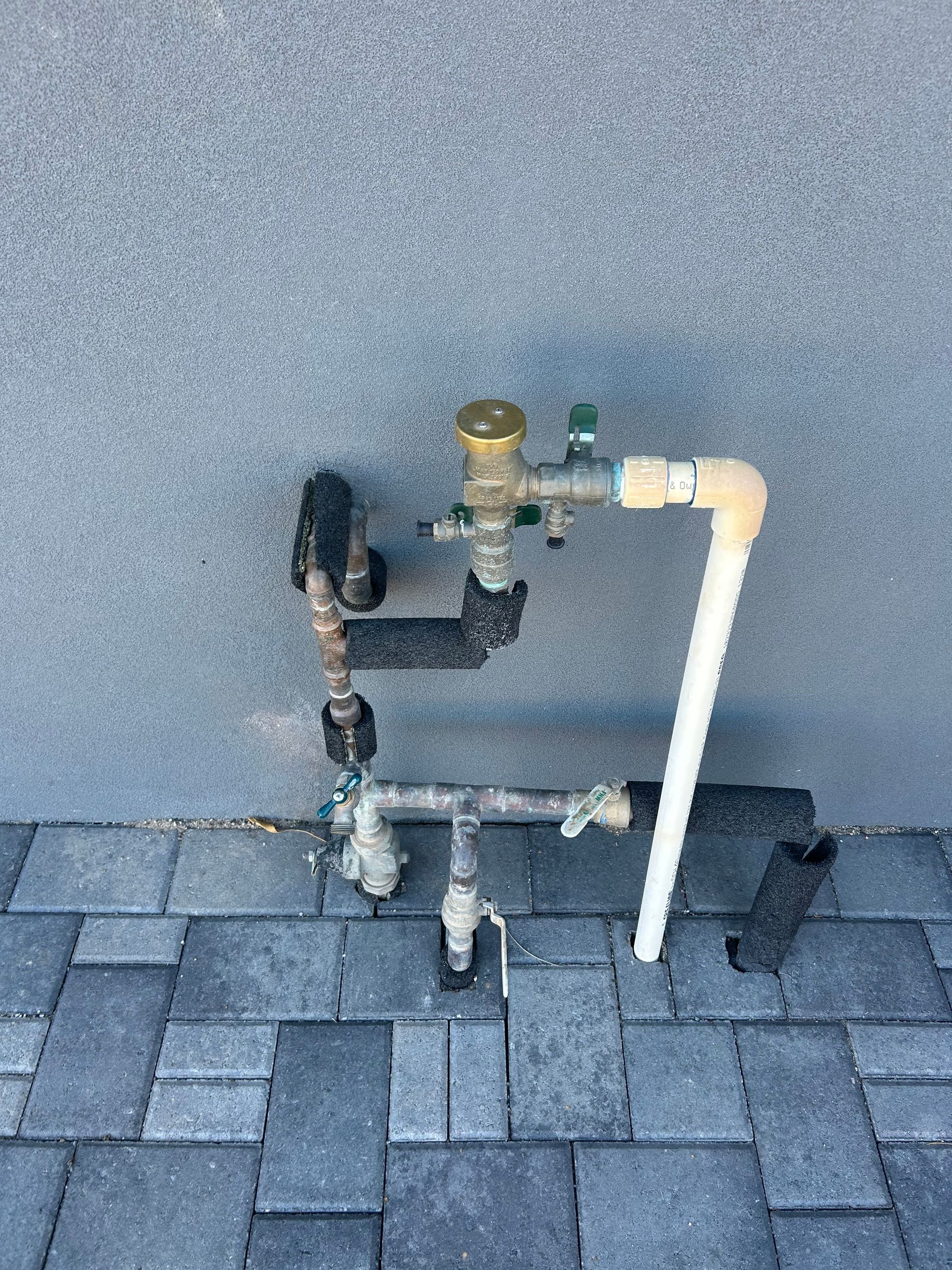 Water pipes and valves mounted on a building, including a backflow preventer.