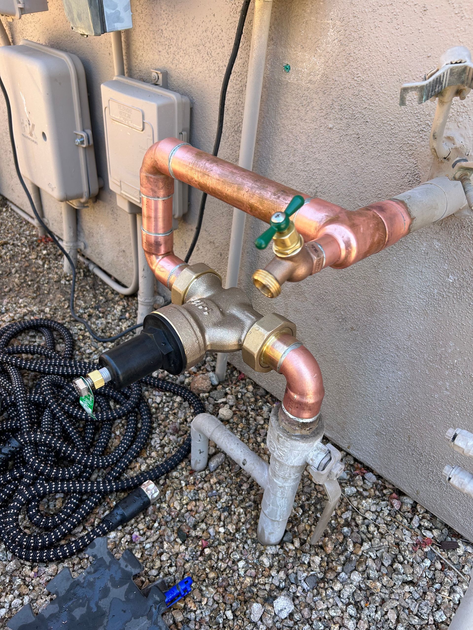 Copper plumbing and spigot attached to a house, with a black garden hose connected.