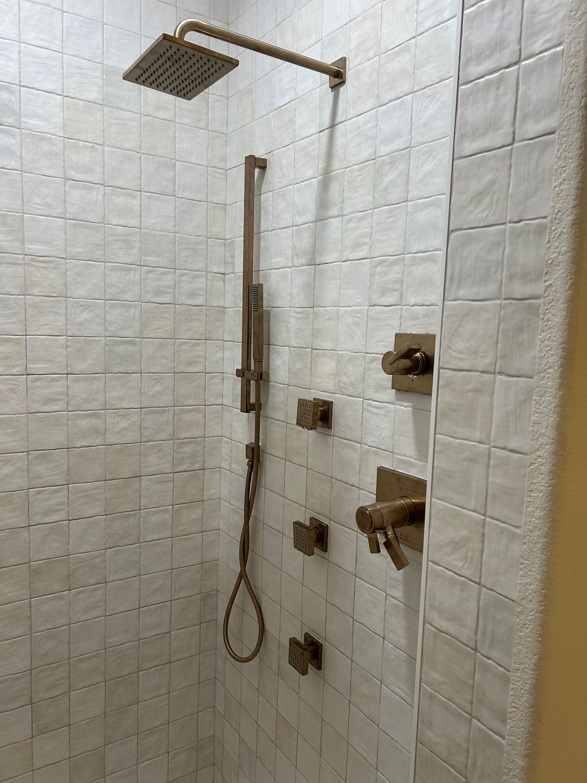 Bronze shower fixtures against white tiled wall.