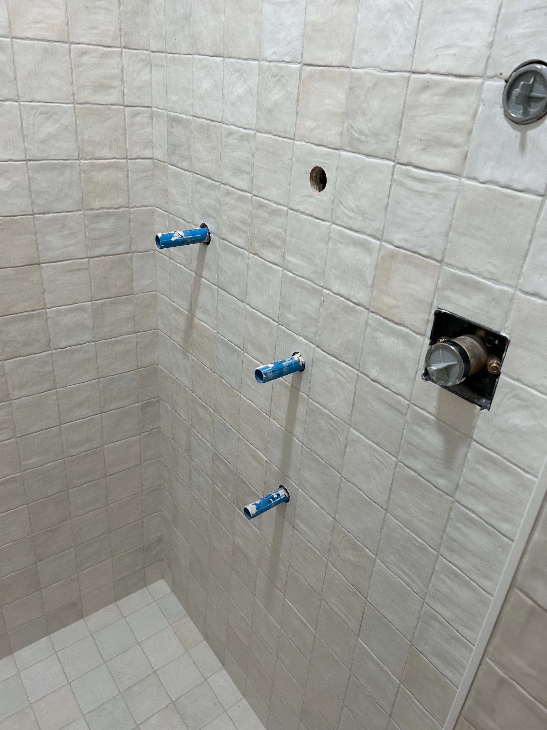 Shower stall with beige tiles; plumbing pipes and showerhead fixtures are installed.