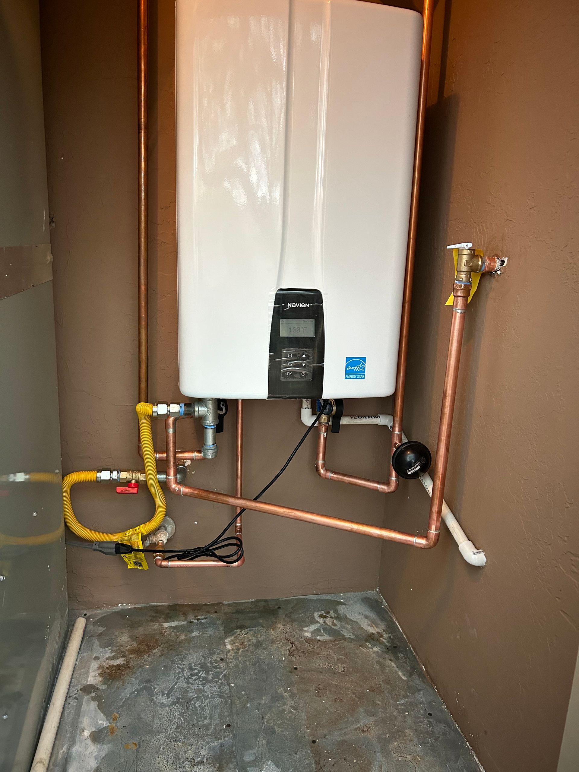 A white, wall-mounted tankless water heater with copper pipes, gas line, and control panel.