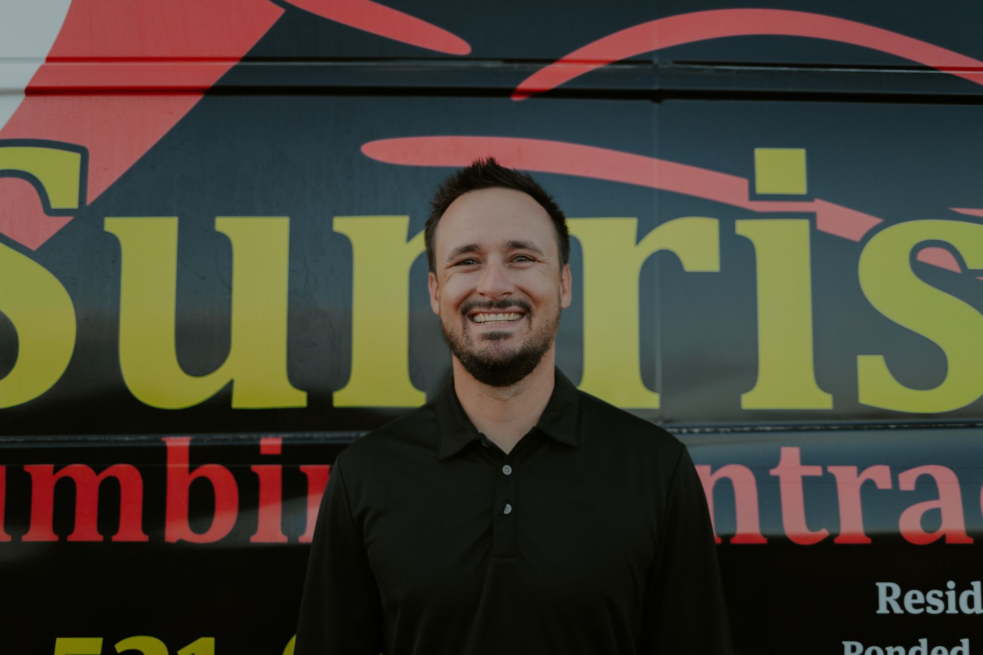 Man smiling in front of black vehicle with red and yellow 