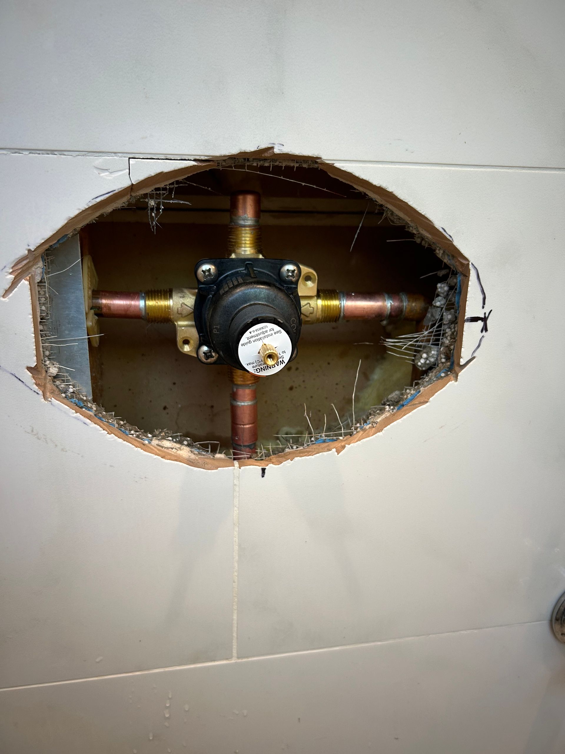 Shower valve plumbing exposed in a tiled wall, with copper pipes and a black valve.