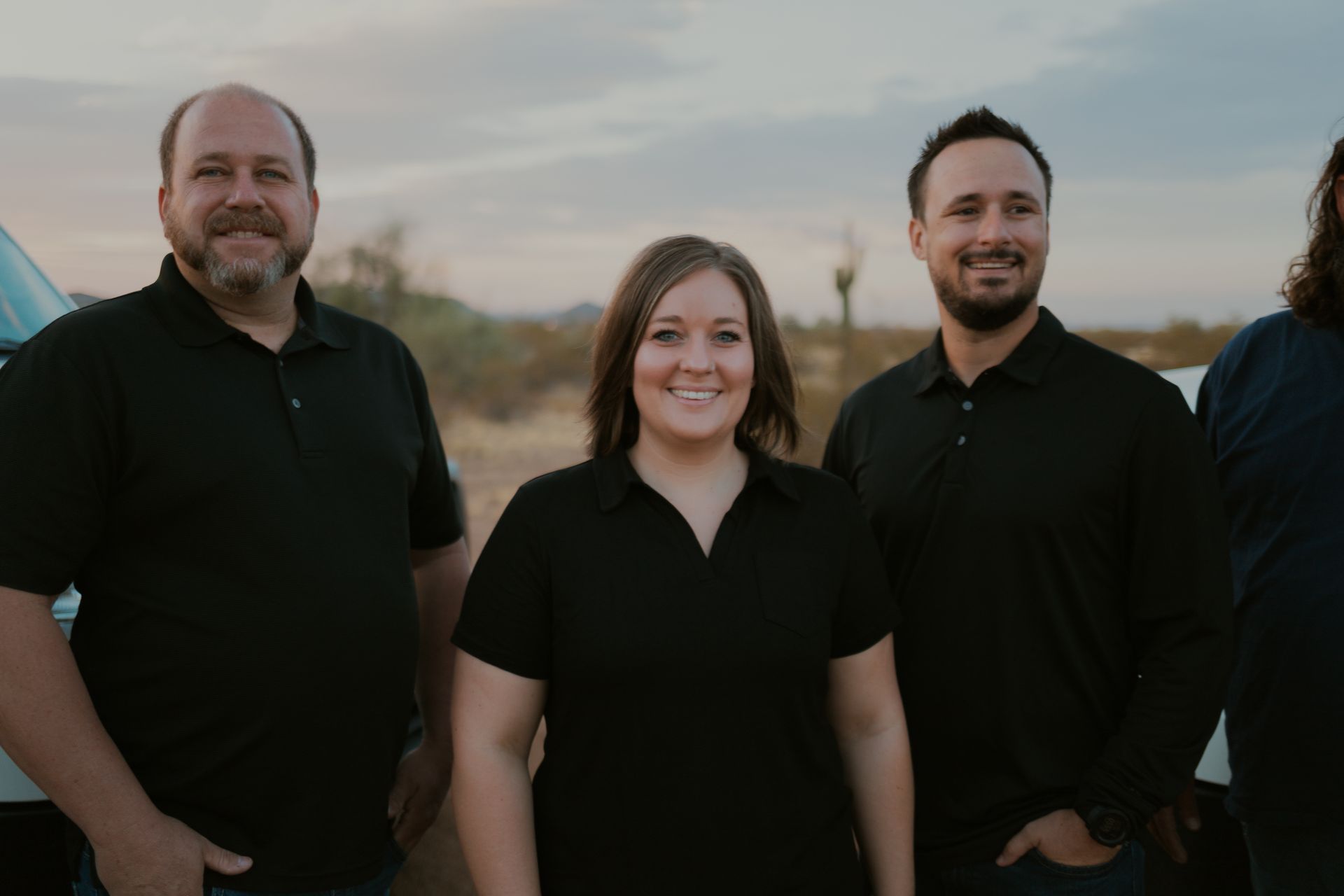 Group of five people in black shirts smiling outdoors in desert.