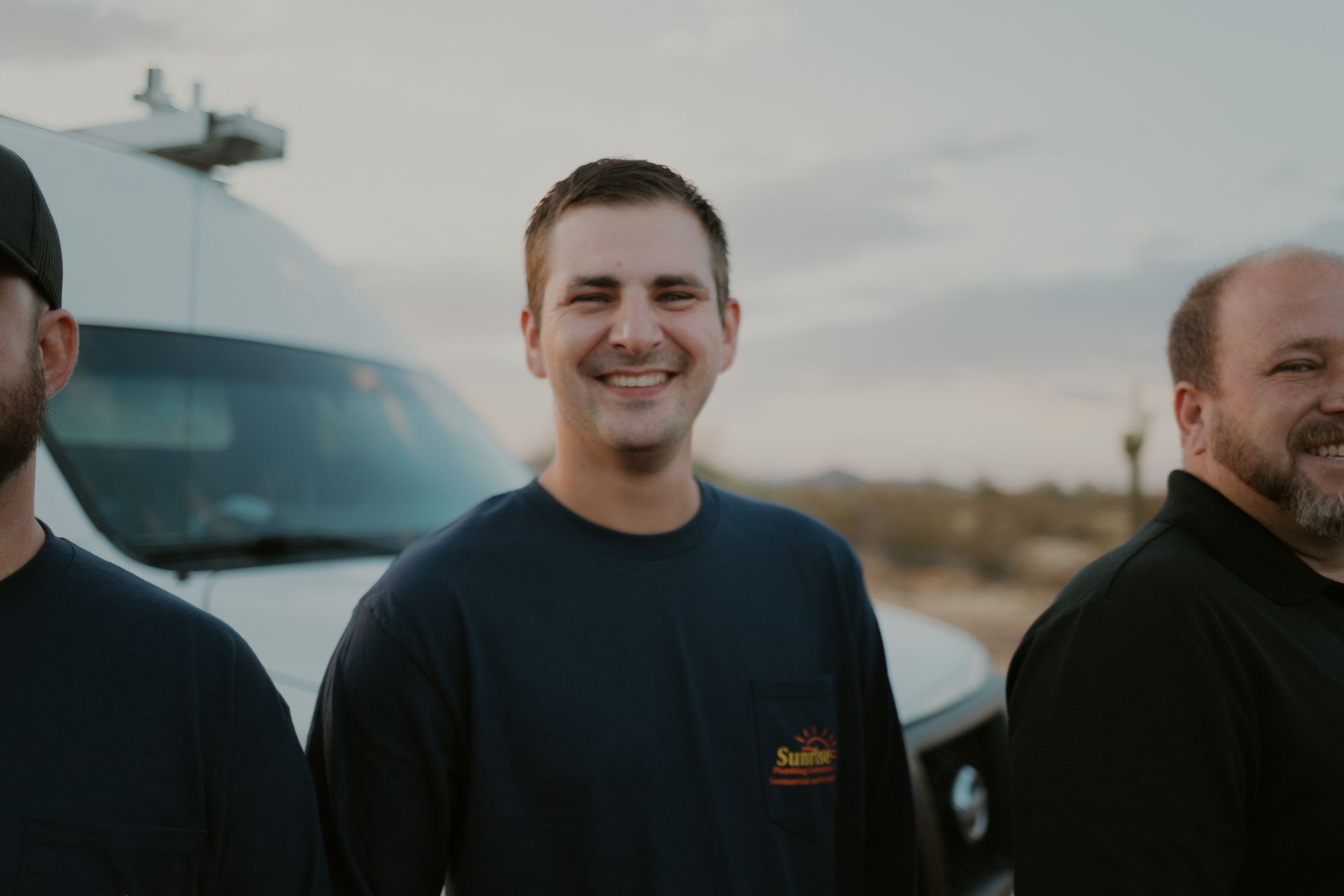 Three men smiling in front of a van in a desert setting.