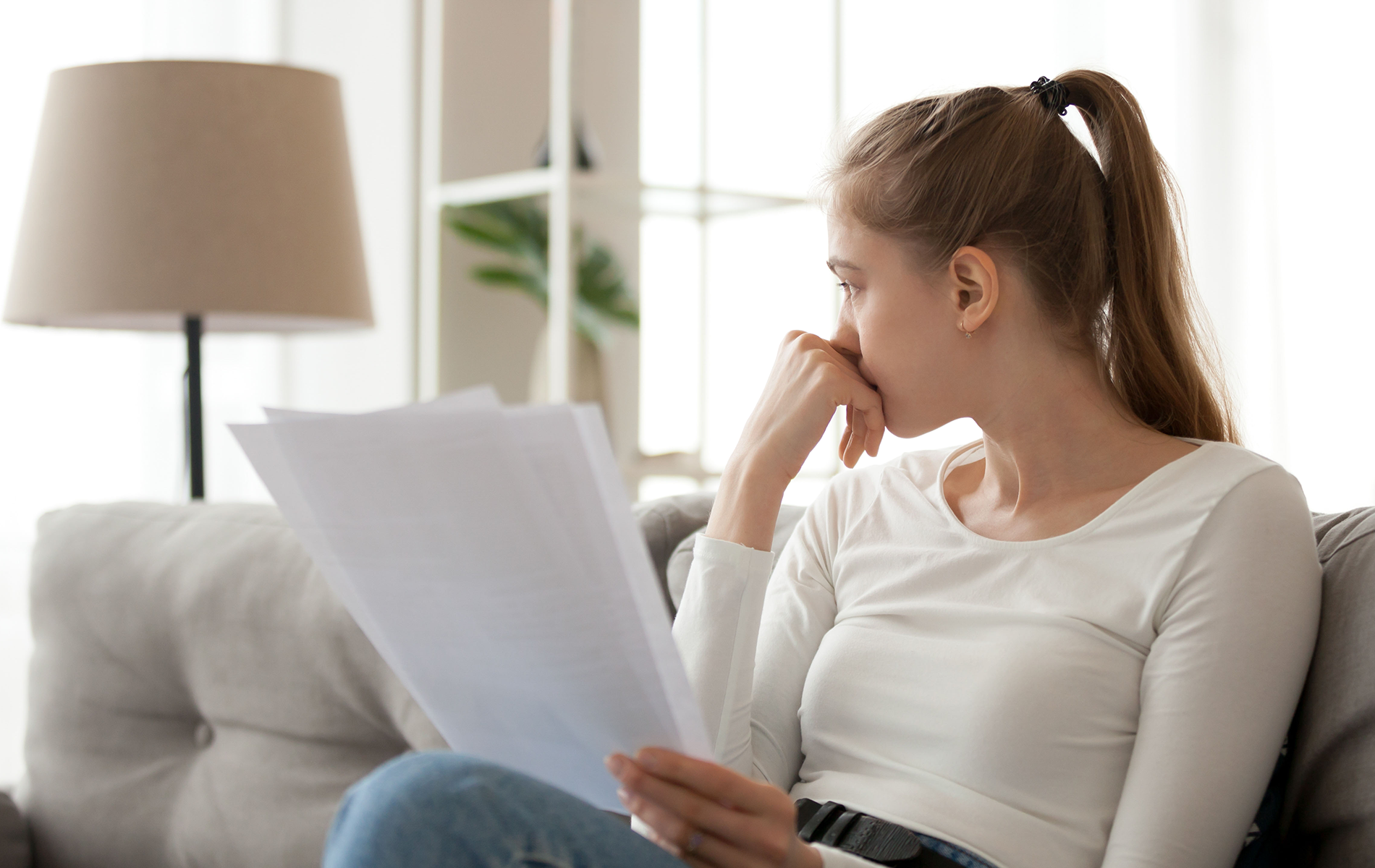 A woman is sitting on a couch reading a piece of paper.