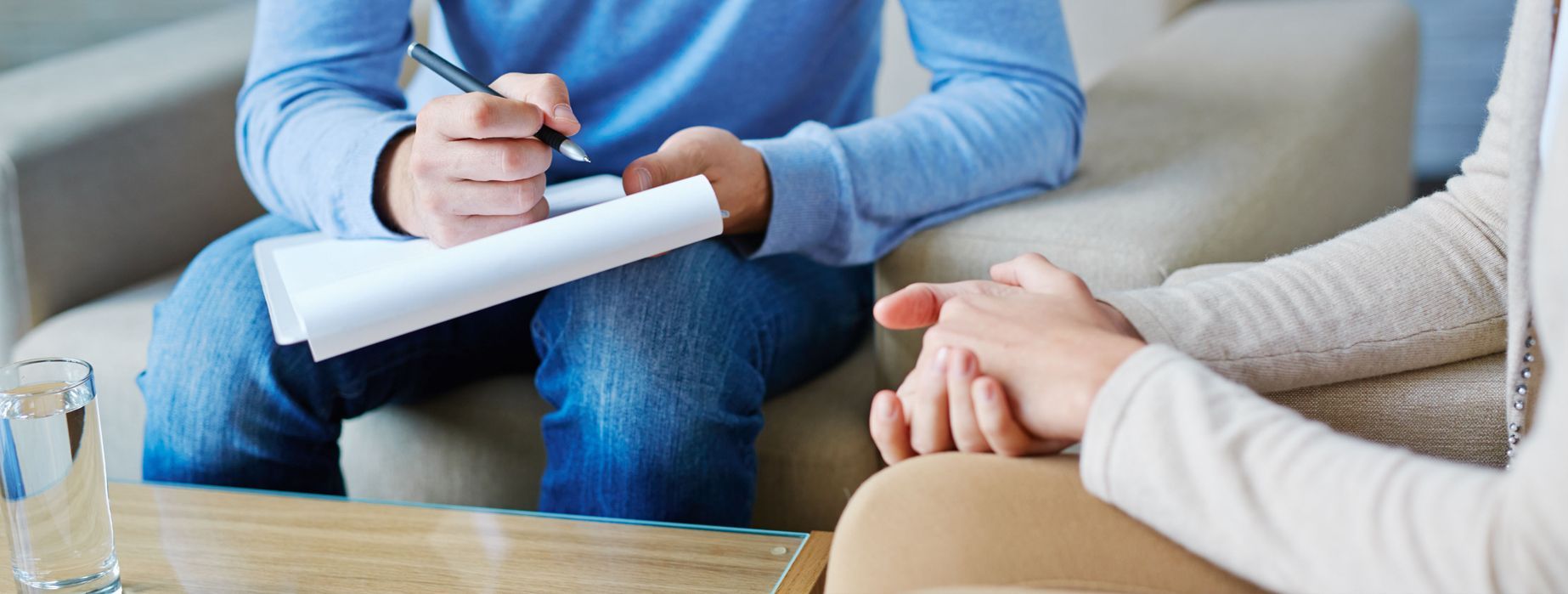A man is writing on a piece of paper while a woman holds his hand.