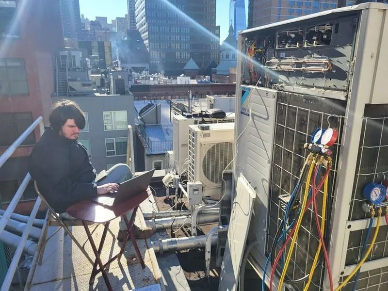Person using laptop on rooftop near HVAC unit in urban setting.