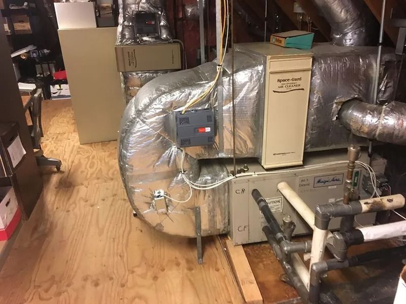 HVAC system in an attic. Includes furnace, ductwork with insulation, and gas lines on a wooden floor.