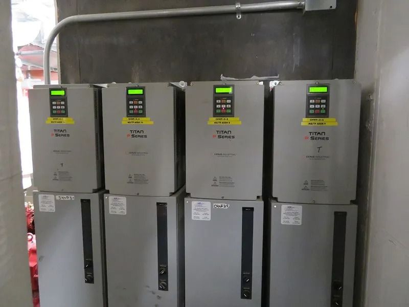 Eight grey electrical control units stacked against a wall with digital displays and labels.