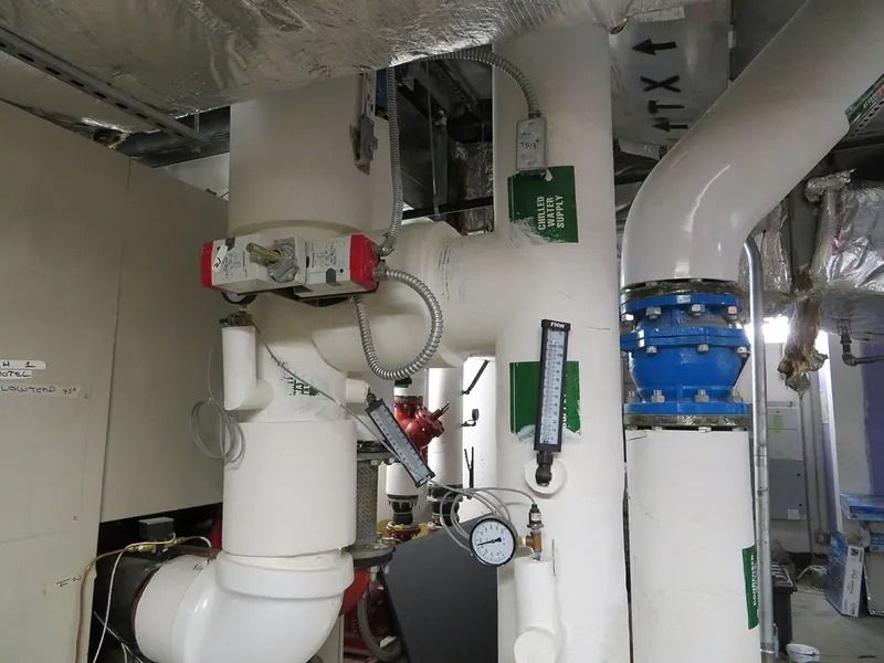 White-insulated pipes with valves and gauges in an industrial setting.