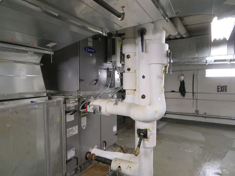 HVAC equipment in an indoor room, including ductwork, pipes, and a Carrier unit. The room is light-colored.