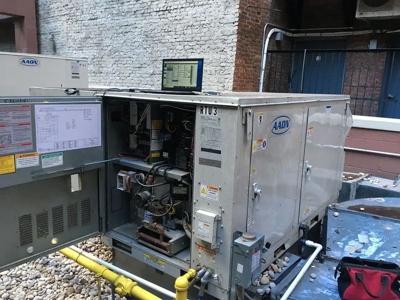 HVAC unit with open panel, a laptop on top, outdoors against a brick wall.