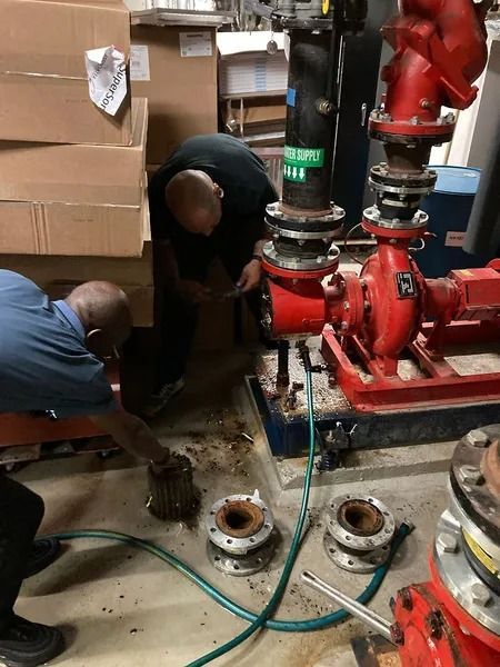 Two men work on red water pump equipment in an industrial setting.