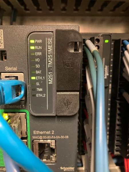 Close-up of a Schneider Electric PLC with illuminated indicator lights and connected Ethernet cables.