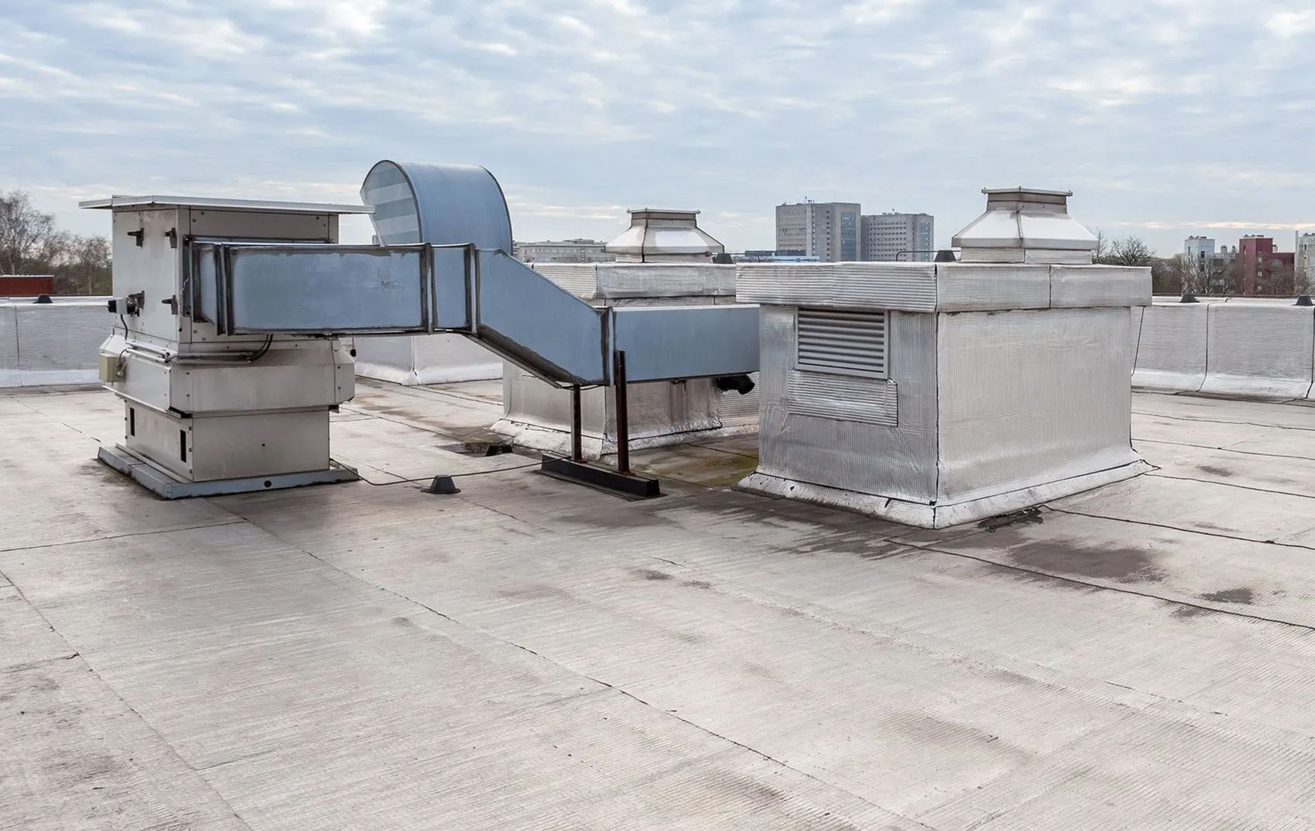 Rooftop HVAC system with metal ductwork on a flat roof under an overcast sky.