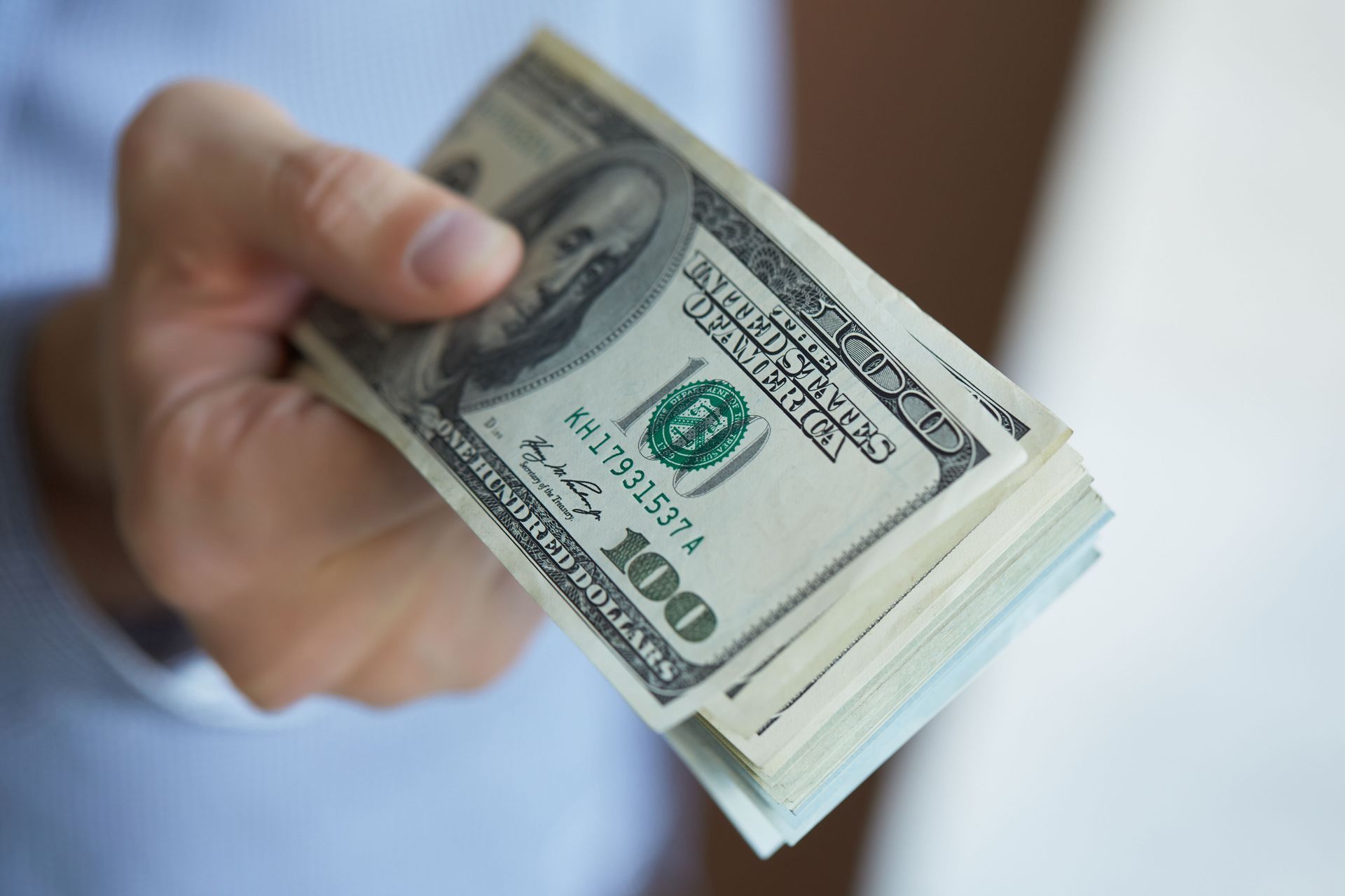 A hand holds out a thick stack of American one-hundred-dollar bills.
