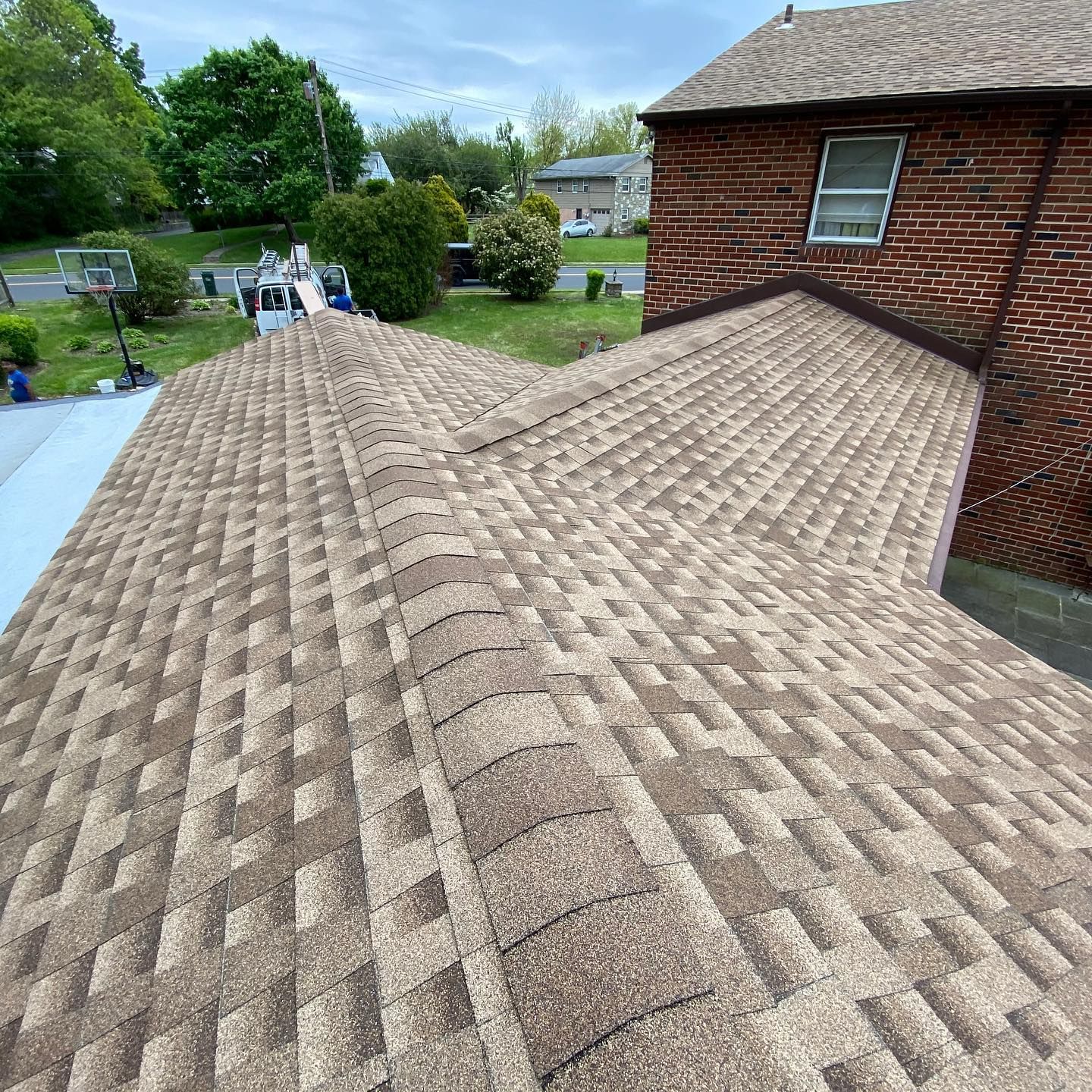 A roof of a brick house with a brown shingle roof.